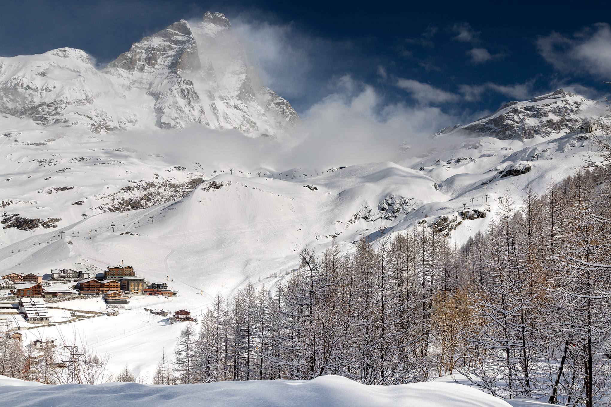 Il Cervino innevato sopra Breuil-Cervinia, con il paese e i larici in primo piano
