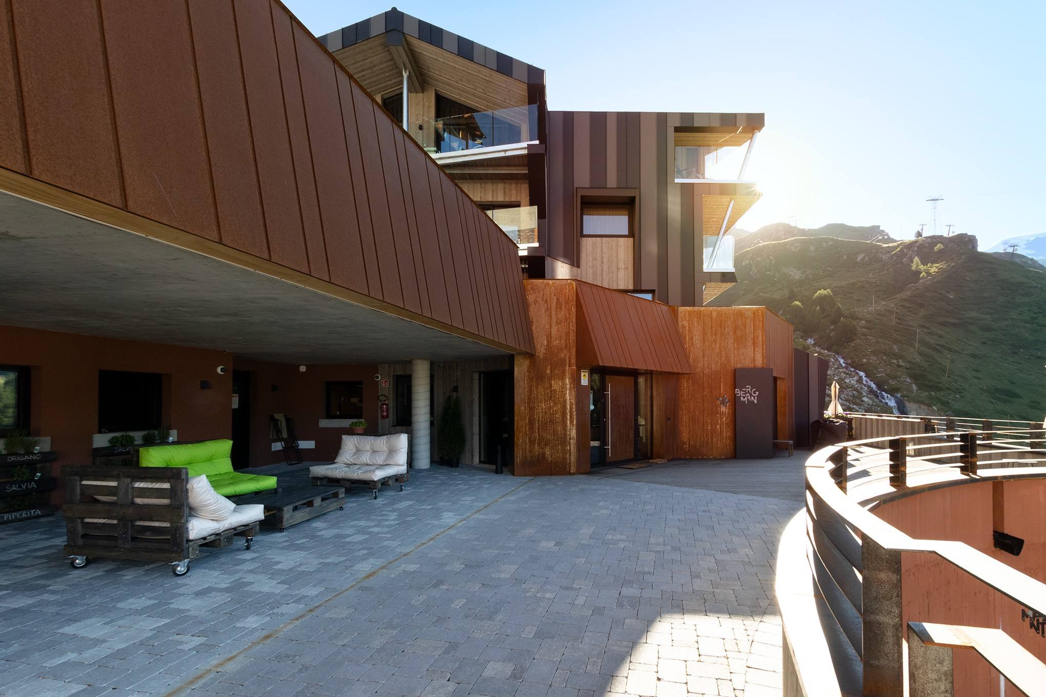 Esterno del Bergman Mountain Hotel in estate, con la terrazza e il sole sulle montagne