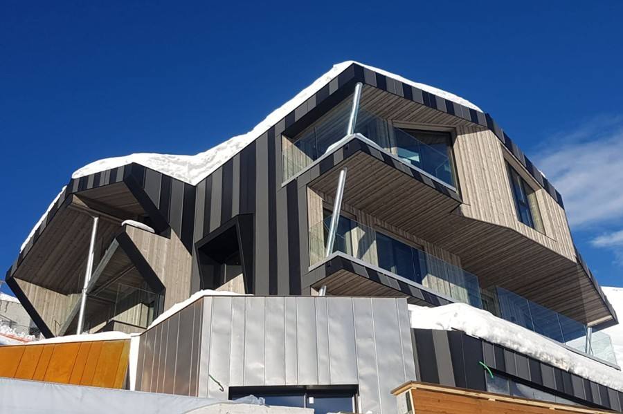 Facciata moderna dell’hotel in legno e metallo sotto la neve e il cielo blu