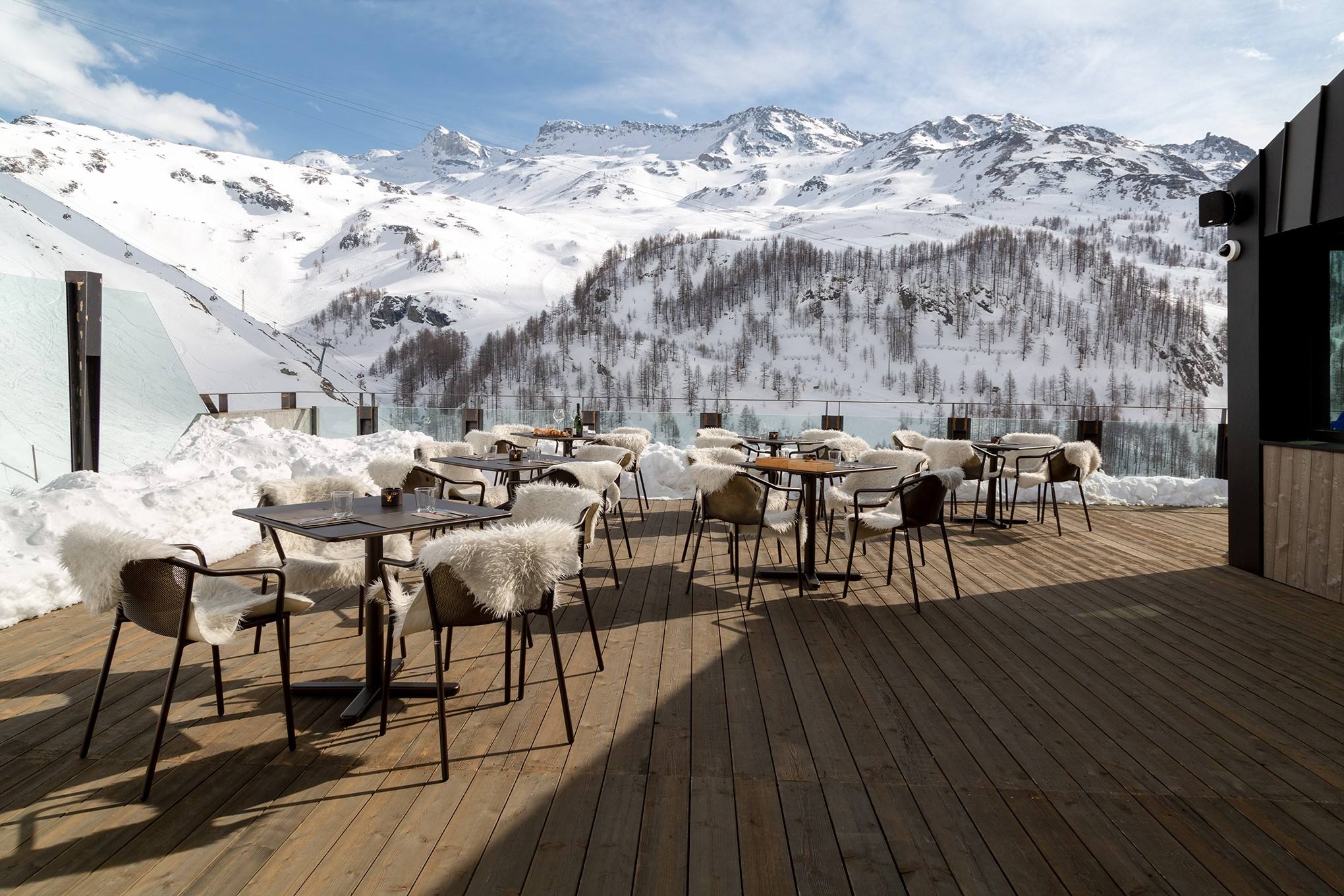 Terrazza in legno dell’hotel con tavoli e pelli, affacciata sulle montagne innevate